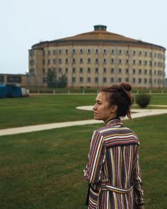 a woman standing in front of a large building on top of a lush green field