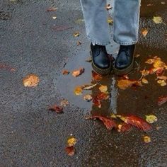 a person standing in the rain with their feet up and wearing blue jeans, holding an umbrella