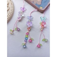 three necklaces with flowers and beads hanging from strings next to a cell phone charger