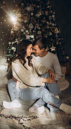 a man and woman sitting in front of a christmas tree