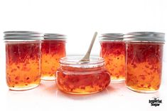 four jars filled with red liquid and a spoon