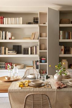 a dining room table is set with plates, bowls and vases in front of bookshelves