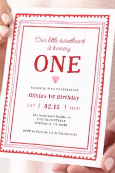 a person holding up a birthday card with the word one on it in red and white