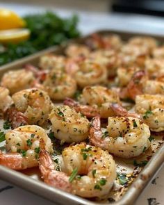 a pan filled with shrimp and garnish on top of a table next to lemon wedges