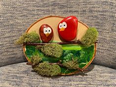 two red birds sitting on top of a wooden plate covered in green moss and trees