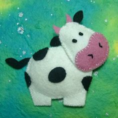 a felt cow with a pink nose and black spots on it's face sitting in the grass