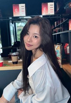 a woman sitting in front of a counter with coffee cups on it's shelves