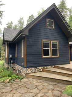 a blue house with steps leading up to the front door and side porch, surrounded by trees