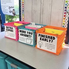 three plastic bins with labels on them sitting on a table in front of a bulletin board