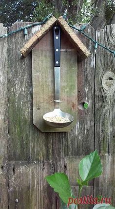 a bird house with a spoon hanging from it's side on a wooden fence