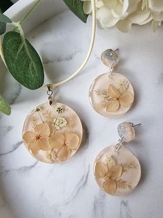 This beautiful pendant contains real dried and pressed flowers set in resin. The floral elements are carefully arranged and set against a beige/off-white background. The flowers in this pendant set are  hydrangea and baby's breath.   This necklace comes with a matching pair of earrings which are approximately 5cms in length and light and comfortable to wear so you can wear this set all day long. This set  perfect for any occasion  and also makes a wonderful gift.  Chain included is beige in colour as seen in the picture and is 17 inches in length PLUS an extender chain of about 2 inches. For more designs check out this listing - https://www.etsy.com/uk/listing/1378658465/pressed-flower-necklace-set-hydrangea?click_key=34f2b55fc842d5b97406155940d8c262a7b231ea%3A1378658465&click_sum=5195d197 Delicate Beige Jewelry Gift, Delicate Beige Jewelry For Gifts, Beige Delicate Jewelry Gift, Pressed Flower Necklace, Dried And Pressed Flowers, Romantic Gifts For Her, Romantic Gift, Flower Necklace, Real Flowers