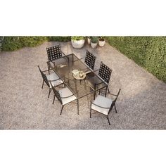 an outdoor dining table and chairs set up on graveled area next to shrubbery