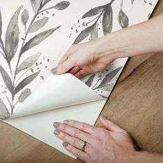 a woman is wrapping up a piece of paper on top of a table with leaves