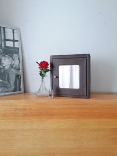 a small vase with a red rose sits on a shelf next to an old photo