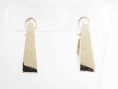 These fancy modern dangle earrings are finished in 14 karat yellow gold. They are secured by an omega closure and face forward for a good view of the triangle design from the side view. The triangles have lovely open spaces at the closure, existing as a design element as well as a functional space for wearing them.Composition: 14 Karat Yellow GoldGeneral Characteristics:Measurements: 1.5 inches x 8.19 mmTotal Gram Weight: 19.6Era: Modern 1970-PresentInscription: 14 KT--ALL PIECES ARE SUBJECT TO Modern Pierced Huggie Earrings For Formal Occasions, Modern 14k Gold Dangle Hoop Earrings, Modern Yellow Gold Dangle Huggie Earrings, Contemporary Yellow Gold Hoop Earrings For Formal Occasions, Modern Hallmarked Huggie Earrings, Formal Minimalist Dangle Huggie Earrings, Minimalist Formal Dangle Huggie Earrings, Minimalist Formal Huggie Dangle Earrings, Modern 14k Gold Rectangular Earrings