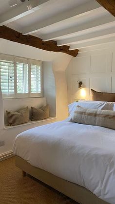 a bed with white sheets and pillows in a bedroom next to a window that has shutters