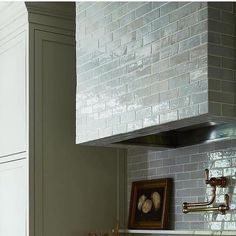 a kitchen with white cabinets and gray tile backsplash, an oven hood over the stove