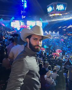 a man wearing a cowboy hat standing in front of an arena full of people at night