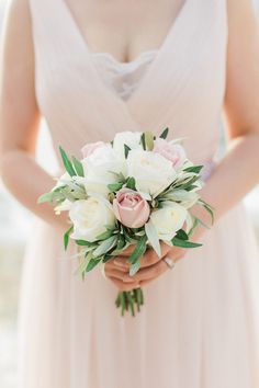 a woman holding a bouquet of white and pink flowers on her wedding day in front of the ocean