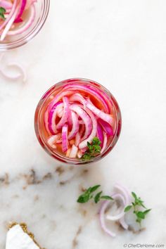 two glasses filled with pickled onions on top of a marble counter next to garlic and parsley