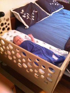 a baby laying in a bed with blue sheets and pillows on it's side