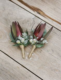 two boutonnieres with flowers and greenery on a wooden surface