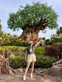 a woman standing in front of a tree at disney's animal kingdom, holding her hand up