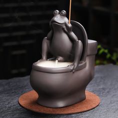 a statue of a frog sitting on top of a toilet with a candle in it