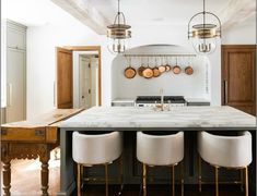 a large kitchen with marble counter tops and stools in front of an island that has hanging pans on it