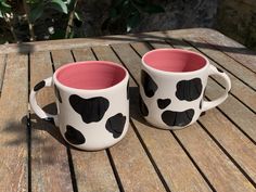 two coffee mugs with black and white spots on them sitting on a wooden table