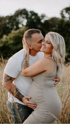 a pregnant couple cuddles in the tall grass