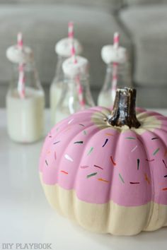 a pink painted pumpkin with sprinkles on it next to some milk bottles