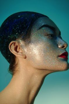 a woman with blue hair and glitter on her face is looking up at the sky