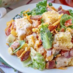 a white plate topped with salad covered in cheese and bacon next to a glass of water