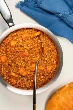 a white bowl filled with lentula and carrots next to a loaf of bread