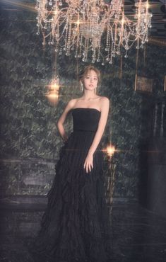 a woman wearing a black dress standing in front of a chandelier