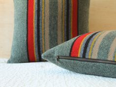 two striped pillows sitting on top of a bed next to each other, one has a zippered closure