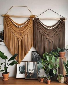 some plants and pictures on a shelf in front of a wall with two hanging macrams