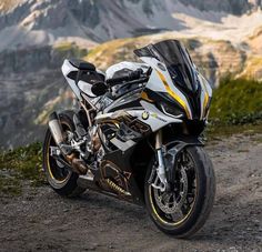 a white and black motorcycle parked on top of a dirt road next to a mountain