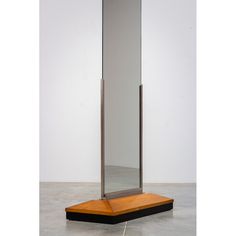 a tall mirror sitting on top of a wooden stand in front of a white wall