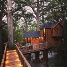 a tree house in the woods with lights on it's porch and stairs leading up to