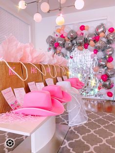 pink and silver hats are on display in front of a large balloon arch with balloons hanging from the ceiling