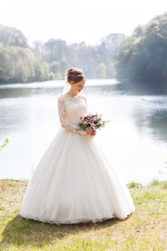 a woman in a wedding dress is standing by the water with her bouquet on her hand