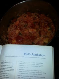 an open book sitting next to a pan filled with food