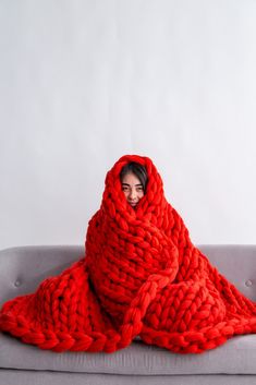 a woman wrapped in a red blanket on top of a gray couch next to a white wall