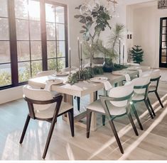 a dining room table with white chairs and a potted plant in the center is surrounded by large windows