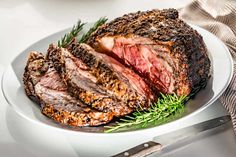 a piece of meat on a white plate with rosemary sprigs next to it