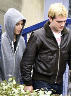 two people walking down the street with one person wearing a hoodie and looking at something