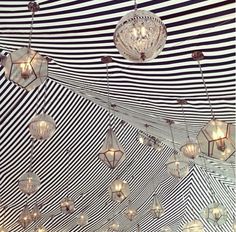 an umbrella with lights hanging from it's sides and striped fabric on the ceiling