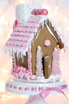 a gingerbread house decorated with icing and pink decorations on top of a cake stand